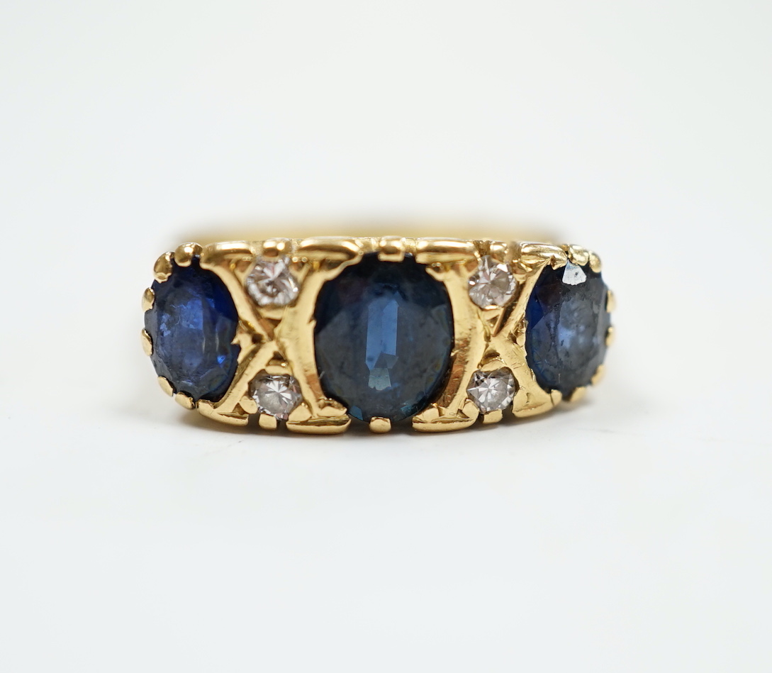 An 18ct and three stone sapphire set half hoop ring, with diamond chip spacers, size O, gross weight 6.2 grams.